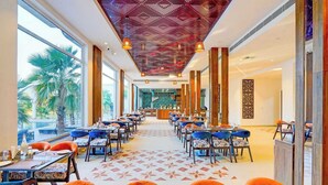 A spacious restaurant with high ceilings, large windows, and a patterned ceiling. Tables are set with chairs, and a counter is visible in the background. - Sunday Resort & Spa Manesar Gurugram (Taoru)