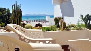 A beach view with a white building, cacti, and a chair. - Mar Esmeralda Apartment (Alcúdia)