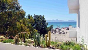 A beach view with cacti, a pier, and mountains in the distance. - Mar Esmeralda Apartment (Alcúdia)
