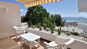 A balcony with white plastic chairs and a table, overlooking a beach with cacti and a clear sky. - Mar Esmeralda Apartment (Alcúdia)