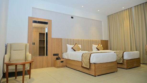 Habitación de hotel moderna con dos camas, una mesita de noche de madera, una silla y un ventanal grande con cortinas.