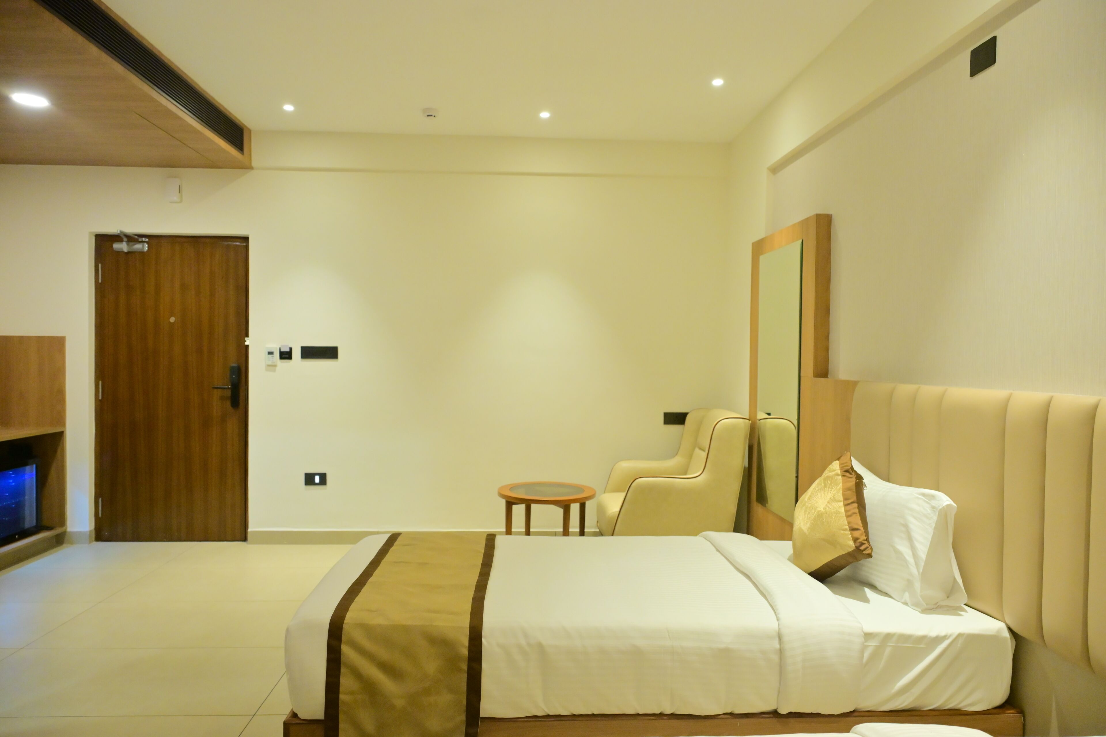 Une chambre d’hôtel avec un lit, une chaise, une petite table, un téléviseur et une porte.