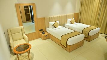 A hotel room with two beds, a chair, a small table, a bedside table with a phone, and a mirror.