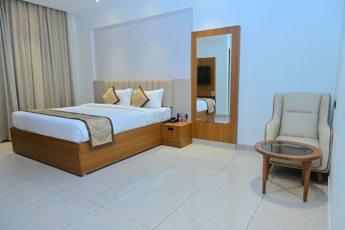 Habitación de hotel con cama, mesita de noche, silla y espejo.