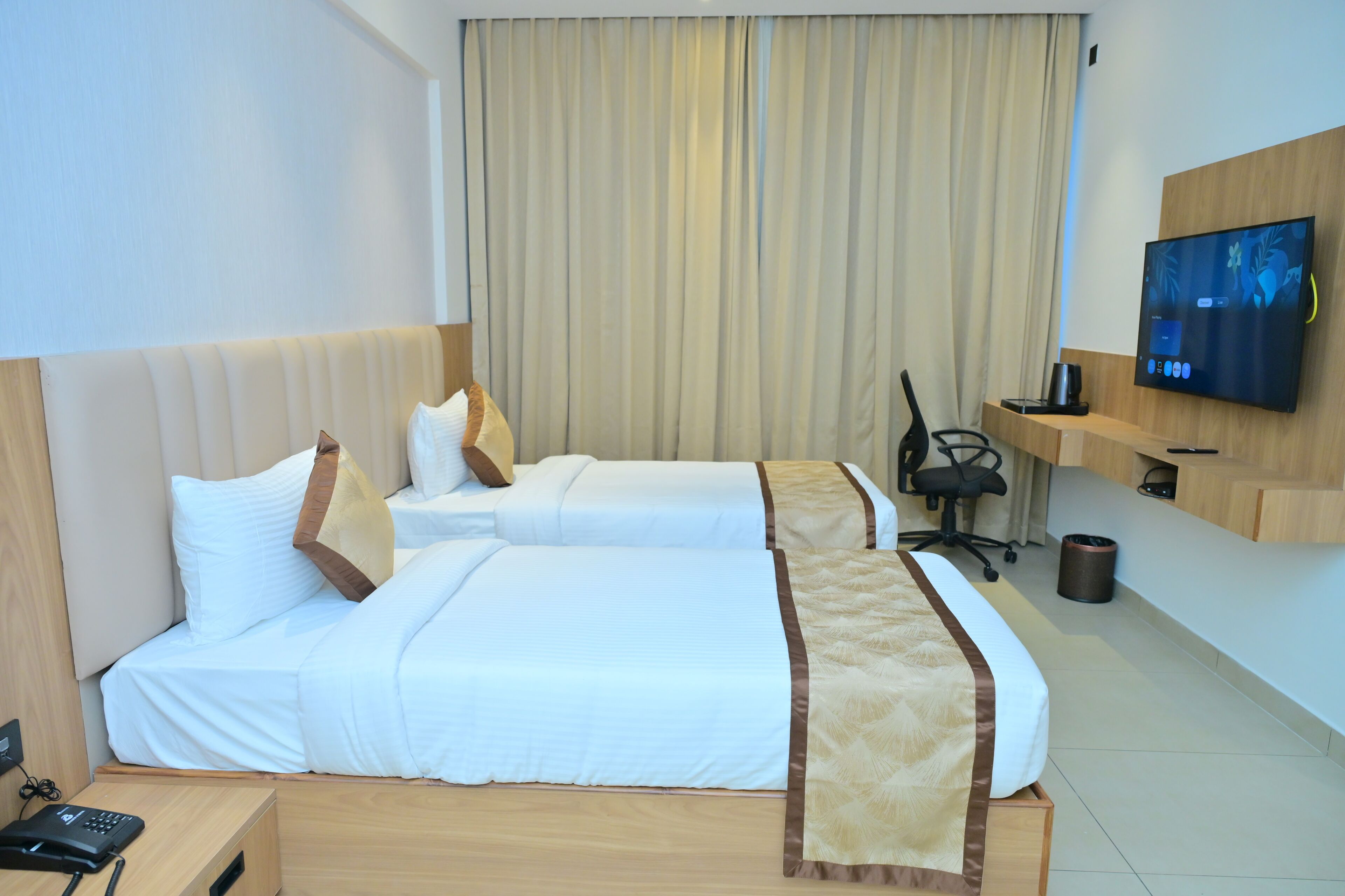 A hotel room with two beds, a TV, a desk with a phone, and a trash can.