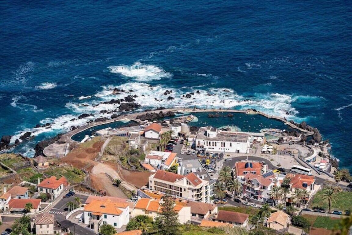 An aerial view of a coastal town with houses, a curved road, and the ocean.