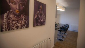 Een gang met twee kunstwerken in lijsten aan de muur, een zithoek met een tafel en stoelen, en een radiator op de vloer.