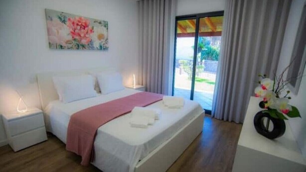 Een slaapkamer met een bed, nachtkastjes, een raam met gordijnen en een schilderij aan de muur.