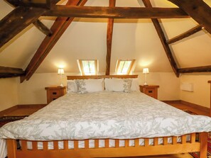 Un dormitorio con techo inclinado, vigas de madera, una cama con colcha estampada, dos lámparas de noche y una ventana con vistas.