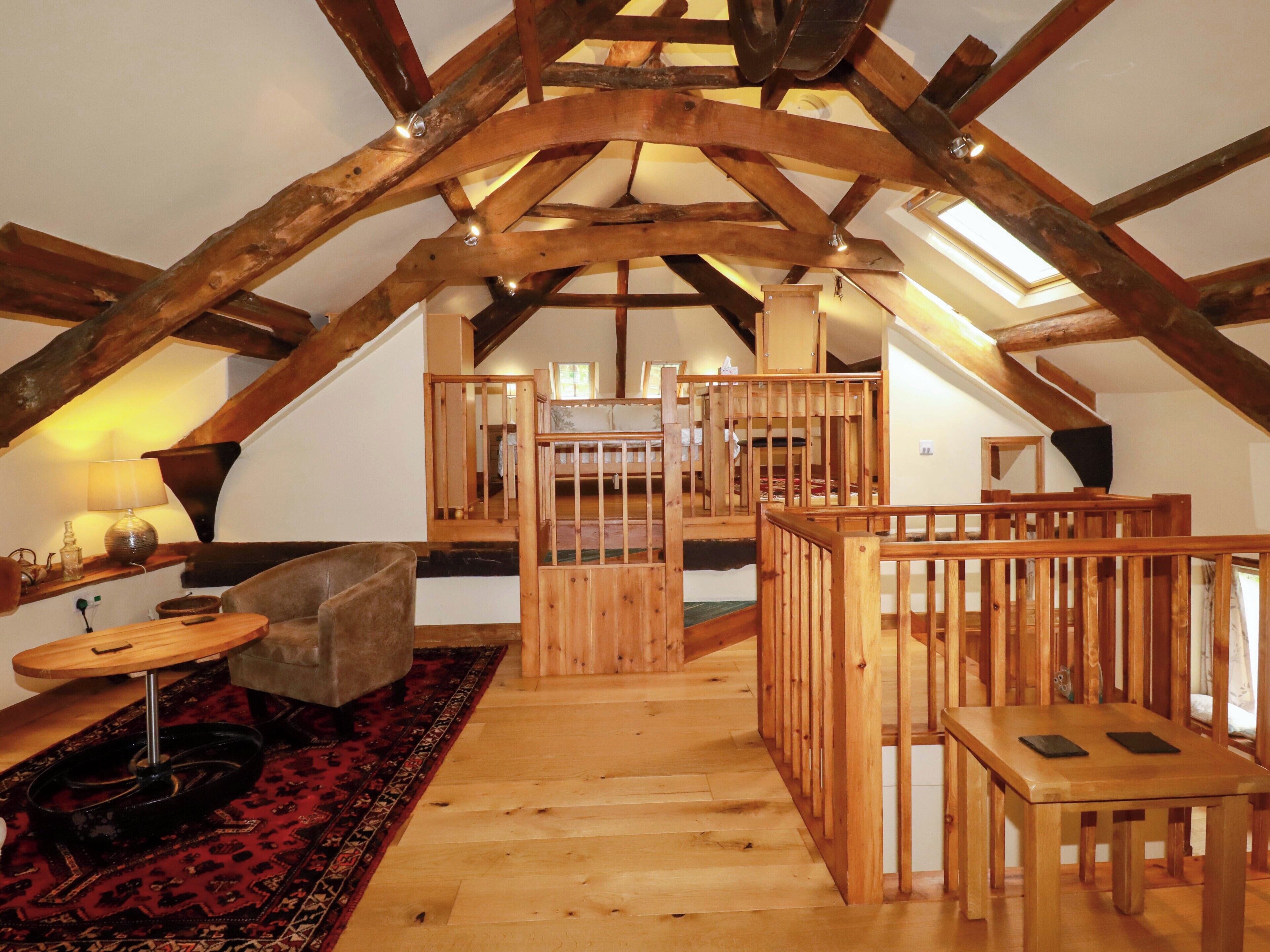 Un espace de vie de style « loft », avec des poutres apparentes, un plafond haut, un escalier central et un coin salon confortable agrémenté d’un tapis.