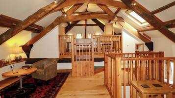 Un dormitorio tipo loft con vigas de madera a la vista, techo alto, una escalera central y una zona de estar acogedora con alfombra.