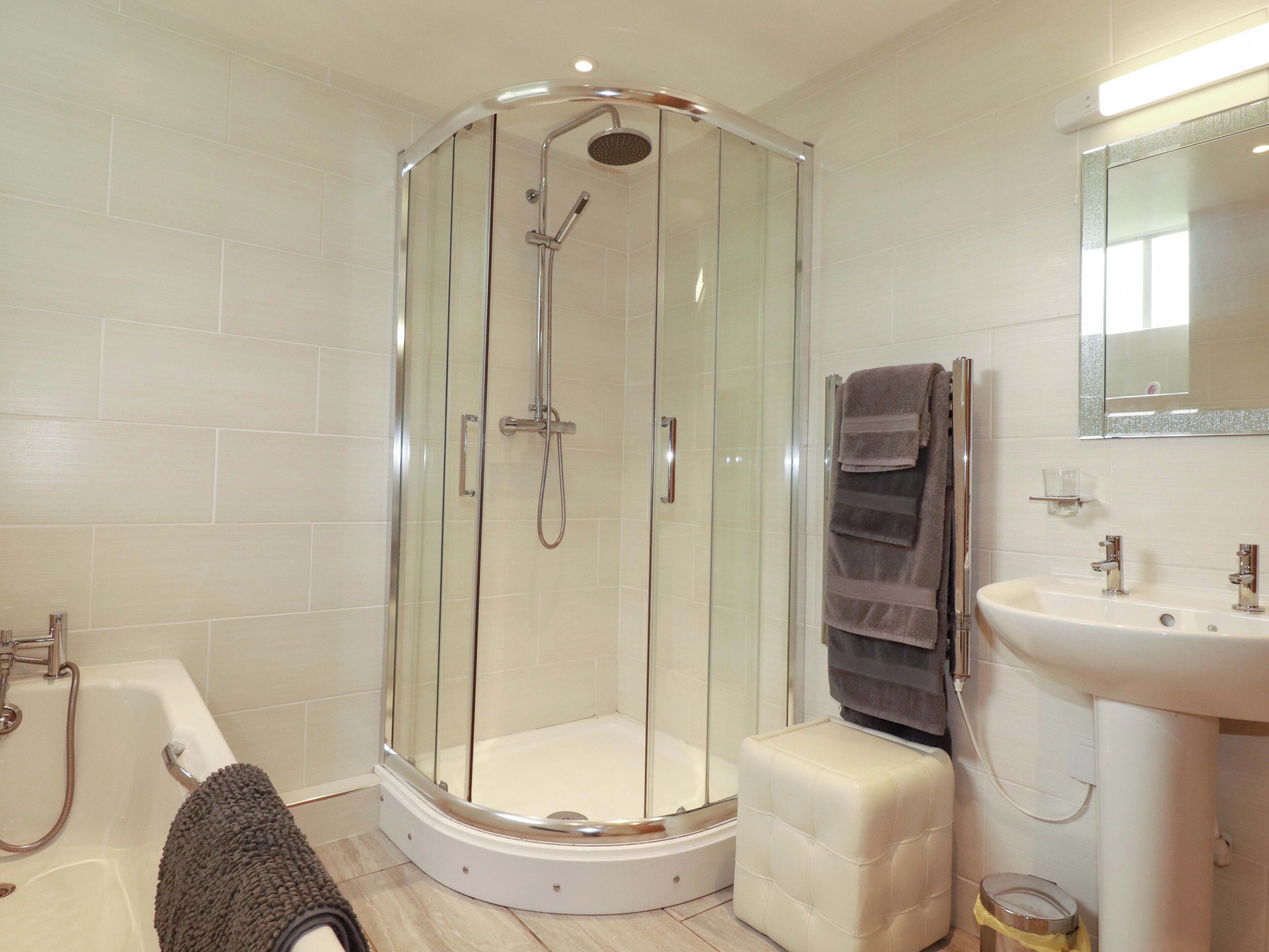 A modern bathroom with a glass-enclosed shower, a bathtub, a vanity with a mirror, and a towel rack.
