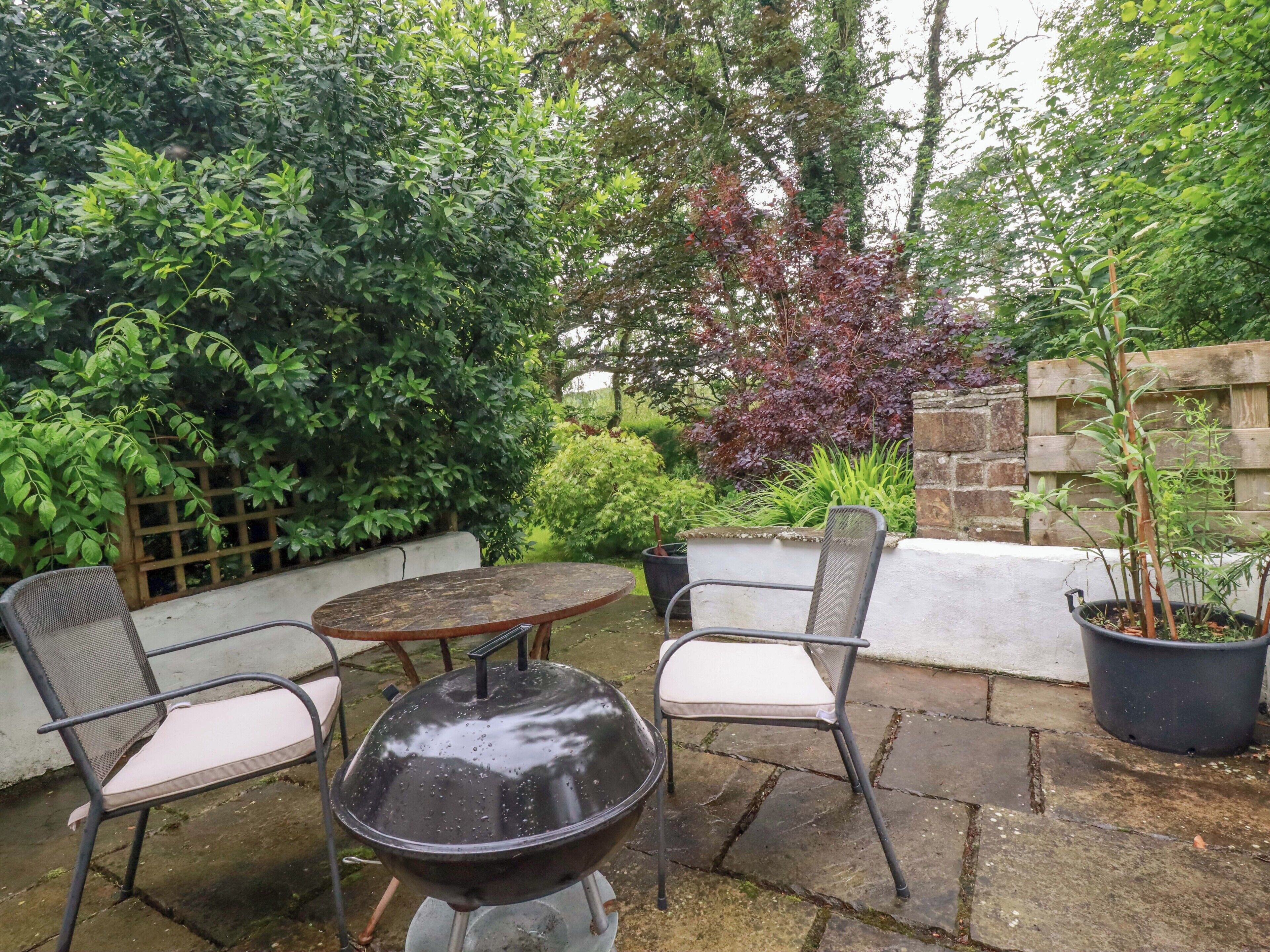 An outdoor patio with a round table, two chairs, and a barbecue grill.