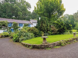 A traditional house with a stone pathway leading to a lawn with a mushroom-shaped stone feature. - The Water Mill at Boyton Mill (Launceston)