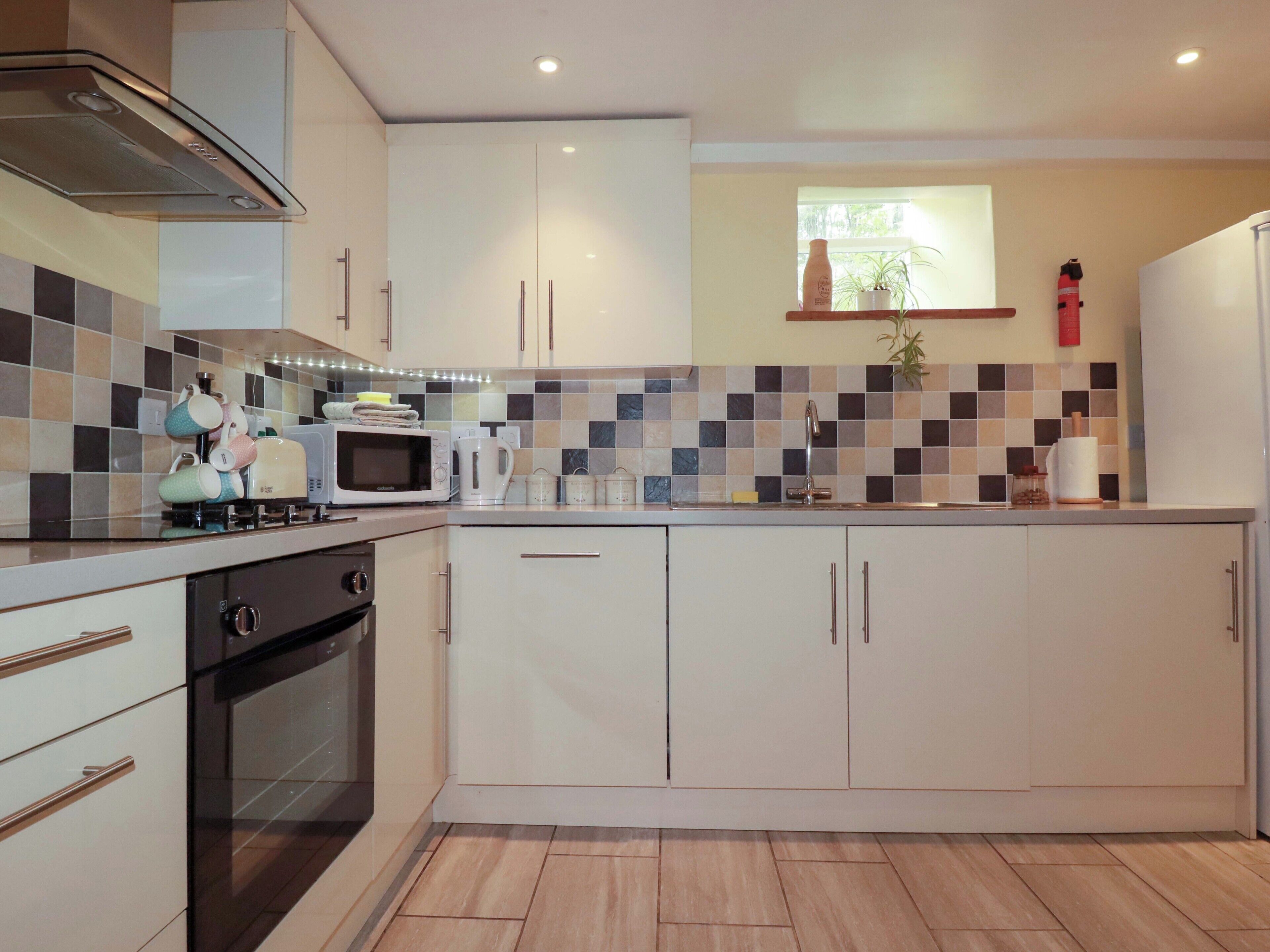 Une cuisine moderne avec des meubles blancs, un four à micro-ondes, une bouilloire et un évier.