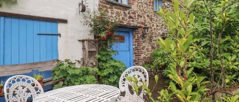 A white metal table and chairs set outdoors, a blue door, and a stone building with a window.
