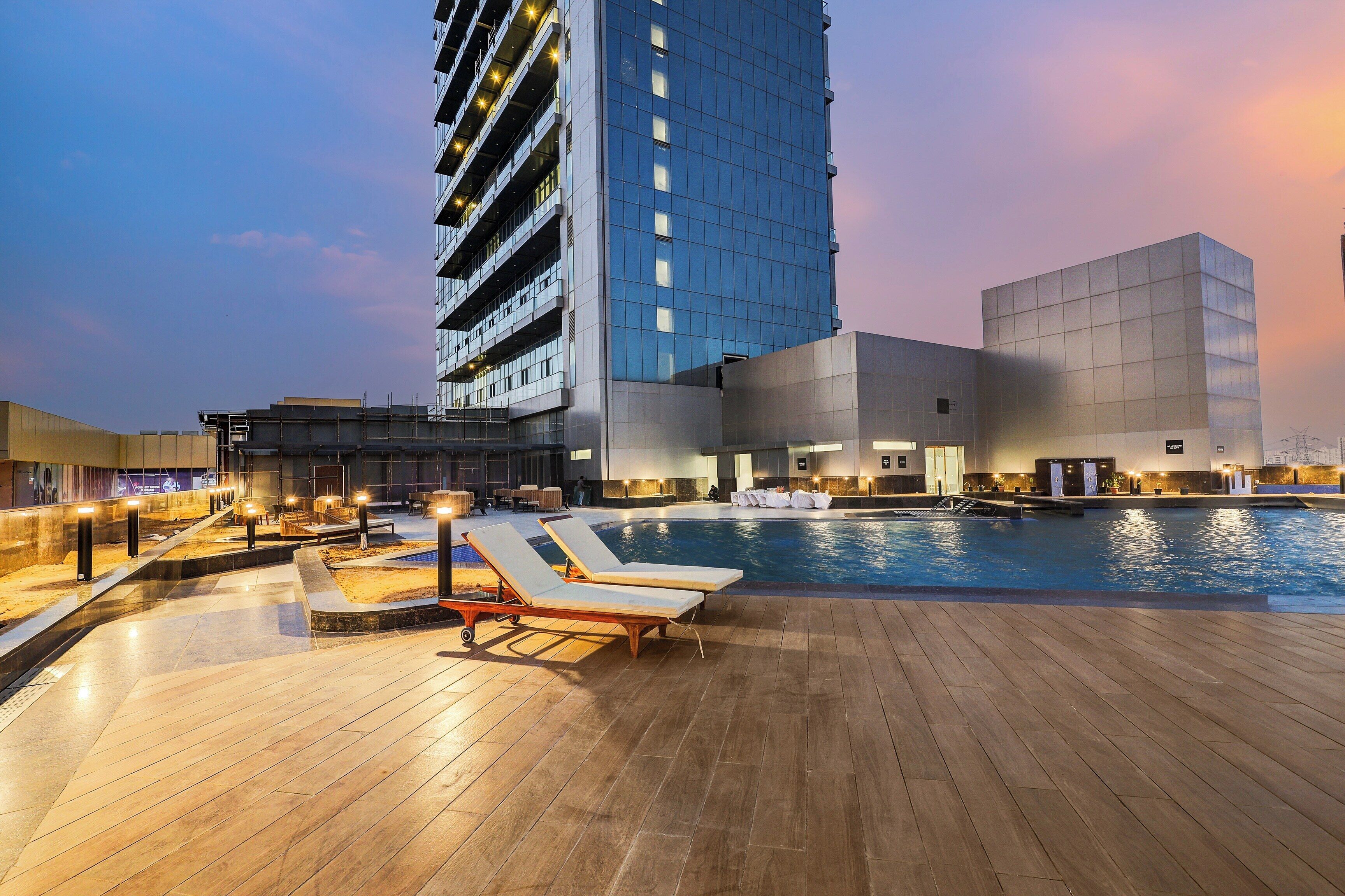 A rooftop pool area with lounge chairs, a swimming pool, and modern buildings in the background.