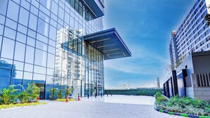 Un edificio moderno con amplios ventanales de vidrio, una plaza pavimentada y algo de vegetación.
