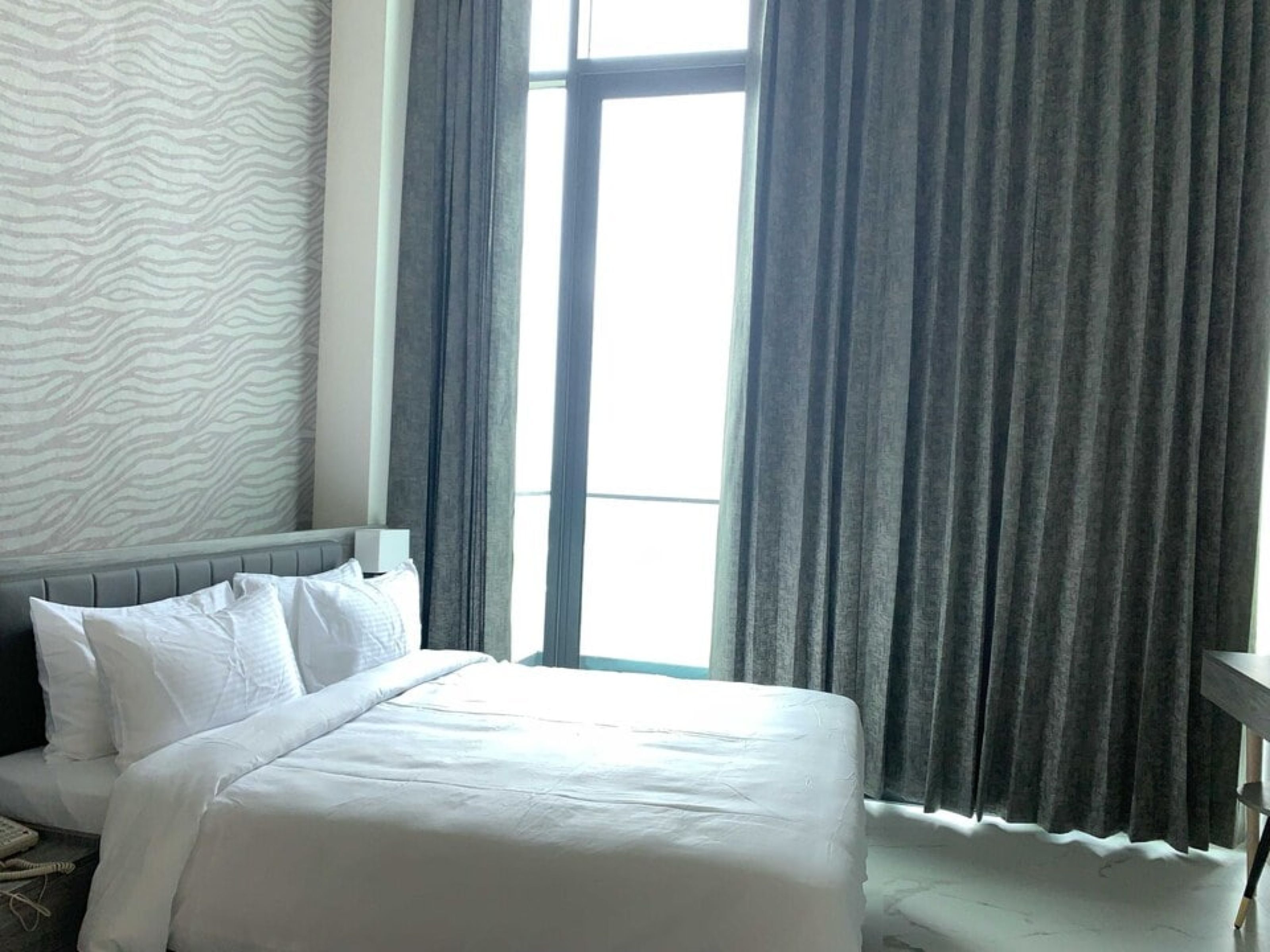 A hotel room with a bed, a window with curtains, and a patterned wall.