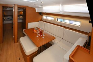 A compact interior with a wooden table, cushioned seating, and a small window. - Sun-Kissed Sailing Adventure in Split, Croatia (Kaštel Gomilica)