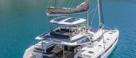 Un voilier doté d’un pont couvert, d’un espace salon et d’une personne se tenant à la proue.