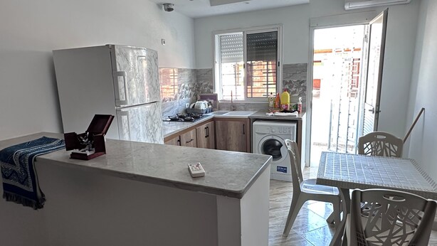 Cocina compacta con refrigerador, lavadora y comedor con sillas.