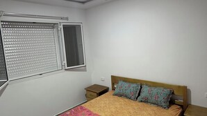 Un dormitorio con cama, dos mesitas de noche, una ventana con persianas y una lámpara en el techo.