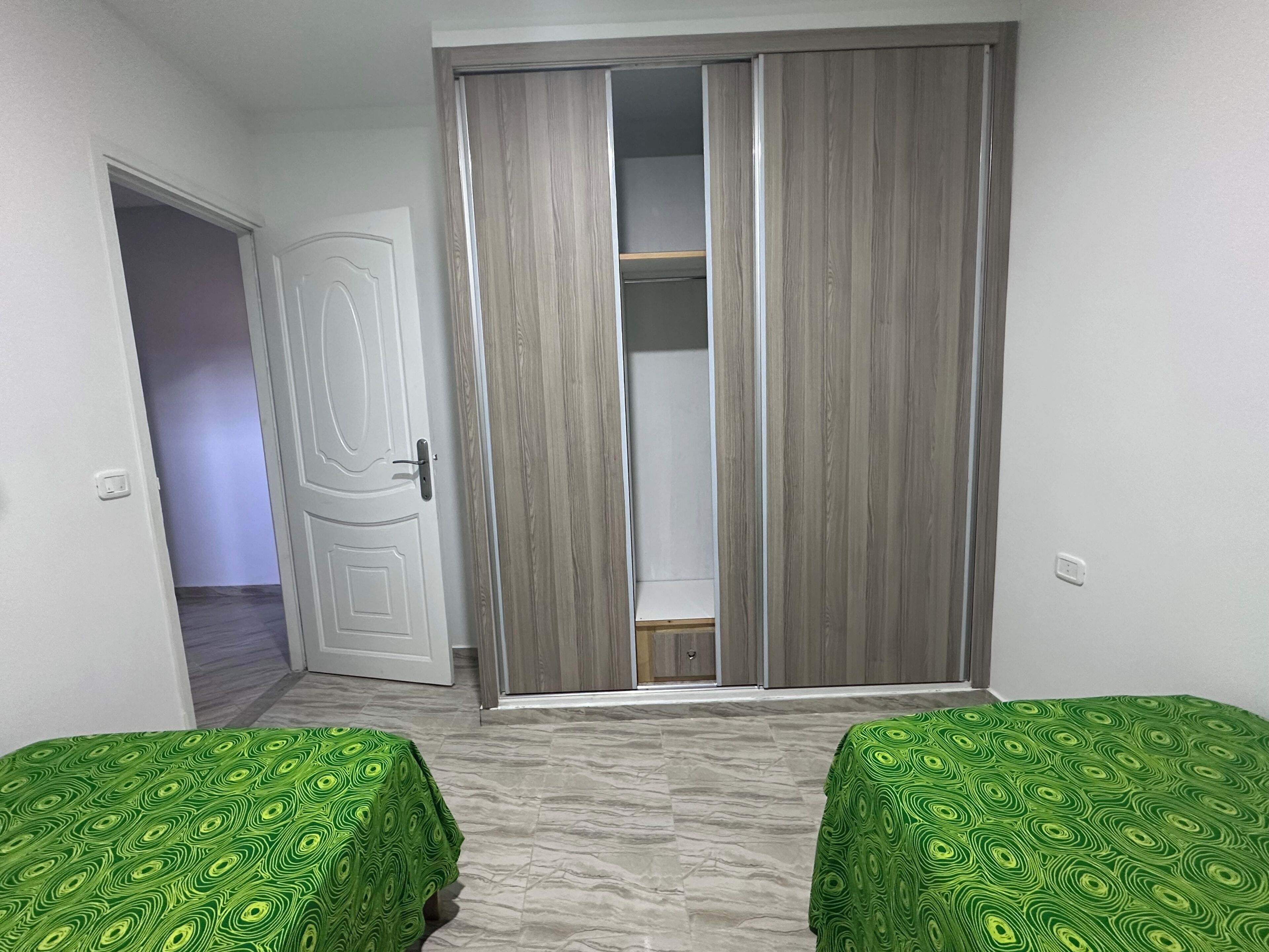 A room with two beds, a wardrobe, and a door leading to another room.