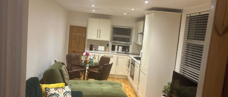 A compact living space with a sofa, dining table, kitchenette, and a TV.