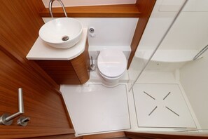 Een kleine badkamer met een witte wastafel, toilet en douche.