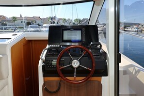 Bedieningspost van een boot, met een stuurwiel, een digitaal scherm en een opgerolde kabel.