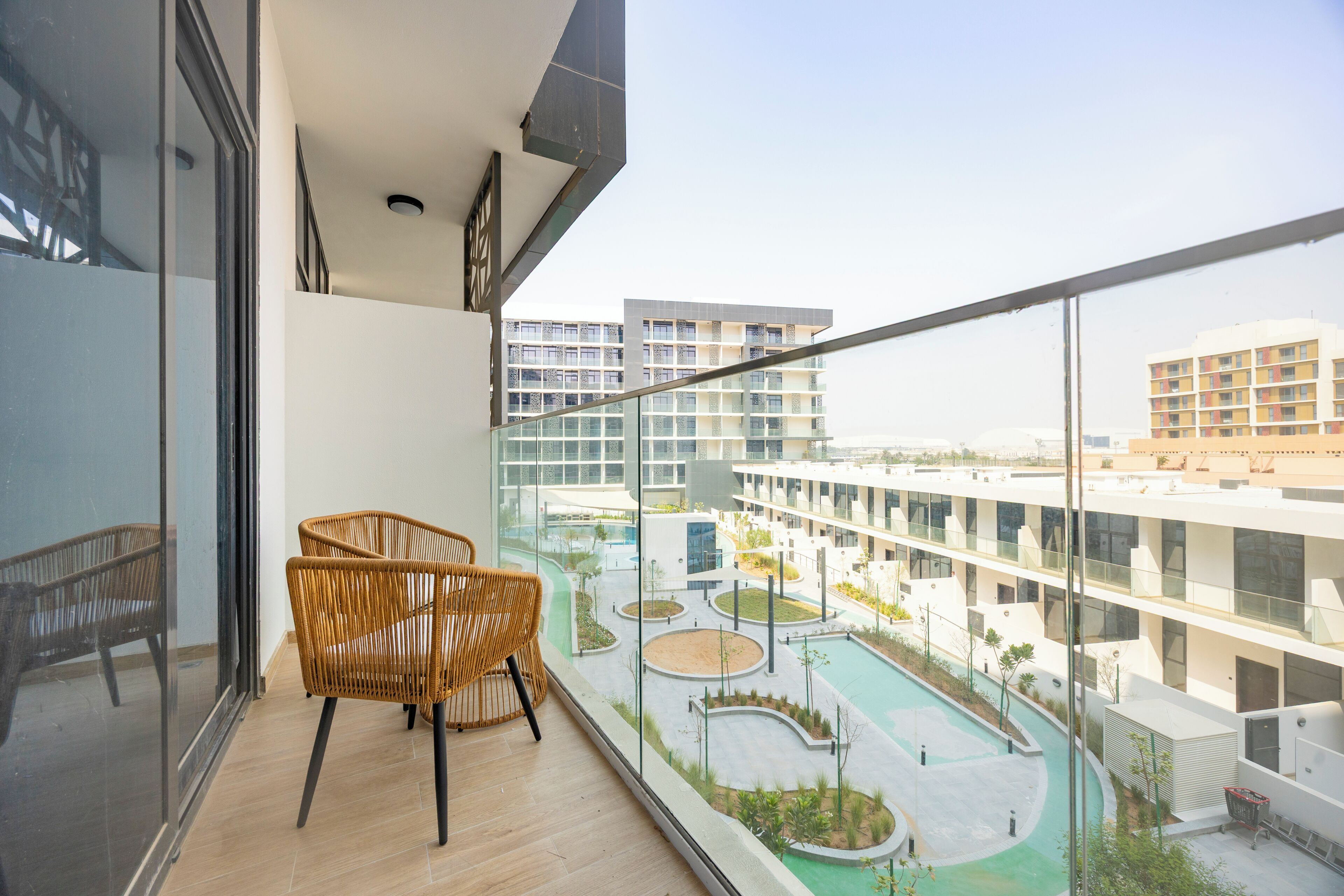 Un balcone con sedie in vimini, vista su una piscina e moderni edifici sullo sfondo.
