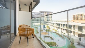 Un balcone con sedie in vimini, vista su una piscina e moderni edifici sullo sfondo.