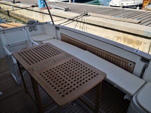 A wooden table with 'Lady Elma' engraved on it, a white cushioned bench, and a view of the dock with boats.