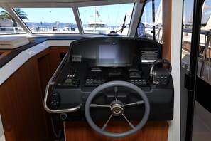 A boat's control station with a steering wheel, navigation screen, and various control panels.