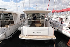 Ein Yachthafen mit vertäuten Booten, darunter eines namens 'BLANDONA' mit einer überdachten Deck und einer Namensschild.