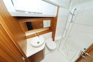 Et lille badeværelse med en hvid vask, toilet og et brusekabine med glas.