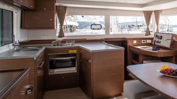 A compact galley kitchen with a built-in oven, a small dining area, and a view of the marina through large windows. - Sun-Kissed Sailing Adventure in Northern Croatia (Punat)