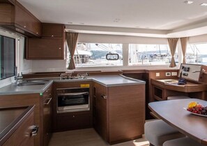 A compact galley kitchen with a built-in oven, a small dining area, and a view of the marina through large windows. - Sun-Kissed Sailing Adventure in Northern Croatia (Punat)