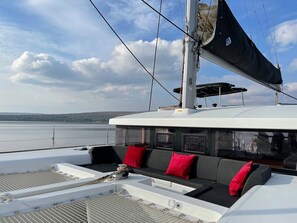Ein Bootsdeck mit Sitzgelegenheit, einem Mast und Blick aufs Wasser.