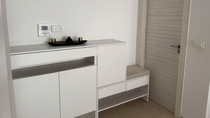 Ein weißes Zimmer mit geschlossener Tür, einer kleinen Ablage mit Thermostat und einem Tablett mit zwei Tassen und einem Topf.