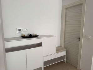 A white room with a closed door, a small shelf with a thermostat, and a tray with two cups and a pot. - Great vacation rental, 2 minutes from the beach—prime location (Sousse)