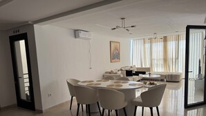 Ein modernes Wohnzimmer mit Essbereich, Deckenventilator und einem großen Fenster mit Vorhängen.