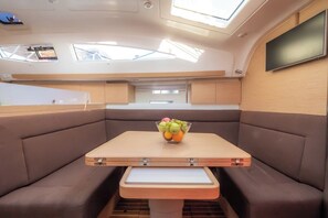 Ein kleines Bootsinnere mit klappbarem Tisch, gepolsterten Sitzen und einer Obstschale.