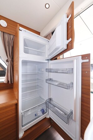 A compact refrigerator with multiple shelves and a freezer compartment, built into a wooden cabinet with a window above. - Sun-Kissed Sailing Adventure in Zadar, Croatia (Biograd na moru)