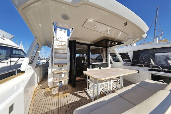 A yacht deck with a table and seating area, a covered section, and a view of other yachts in the background.