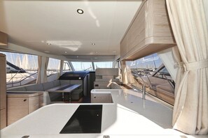 A boat interior with seating, a table, and windows offering views of the marina.