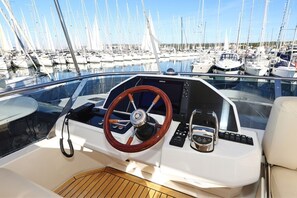 A boat's interior with a steering wheel, control panel, and seating area.