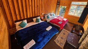 Una cabaña de madera con dos camas, una mesita y un ventanal con vistas al verdor.