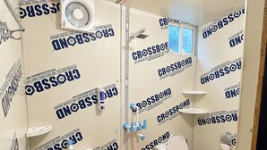 Un baño con inodoro, lavamanos, ducha y un cubo rosa.